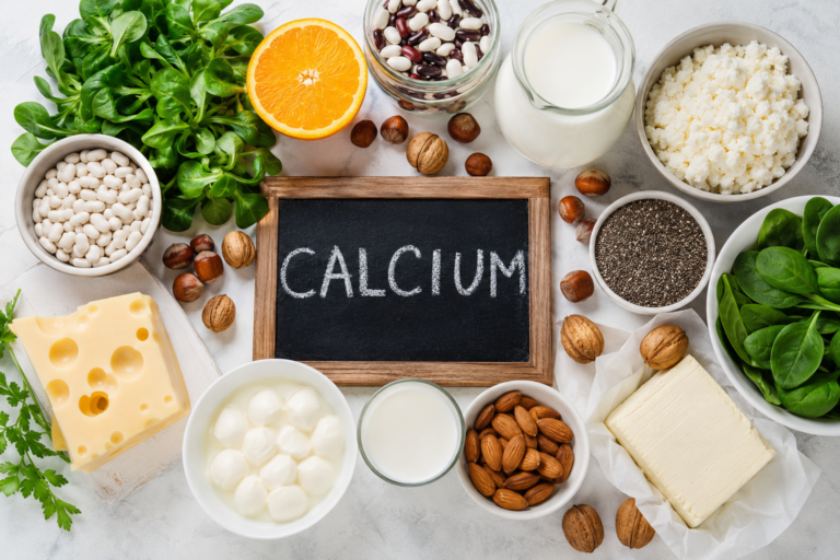 Calcium rich foods including milk cheese yoghurt almonds spinach beans and nuts arranged around a chalk blackboard